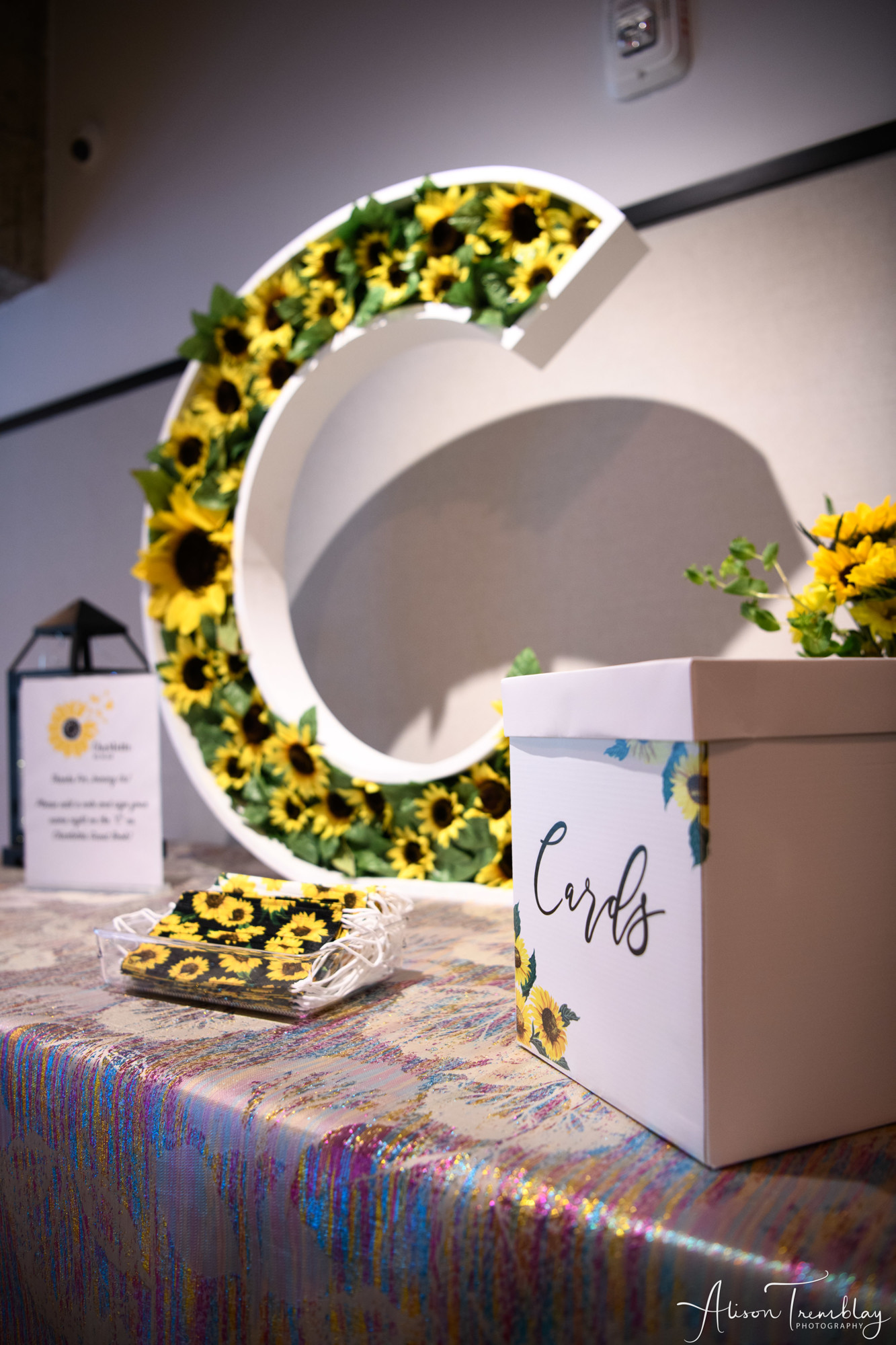Charlotte's sign in letter "C" board filled with sunflowers with sunflower face masks and a sunflower card box at Charlotte's Sunflower and Butterfly Bat Mitzvah Party at Eaton In Washington, DC | Pop Color Events | Adding a Pop of Color to Bar & Bat Mitzvahs in DC, MD & VA | Photo by: Alison Tremblay